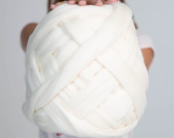 May include: A large, off-white ball of chunky knit yarn. The yarn is thick and soft, with a woven texture. This yarn is suitable for creating large blankets, scarves, or other home decor items.