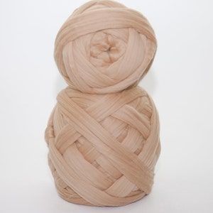 May include: Two large balls of beige yarn are stacked on top of each other against a white background. The yarn is thick and appears to be made of a soft material. The yarn is tightly wound, creating a textured surface.