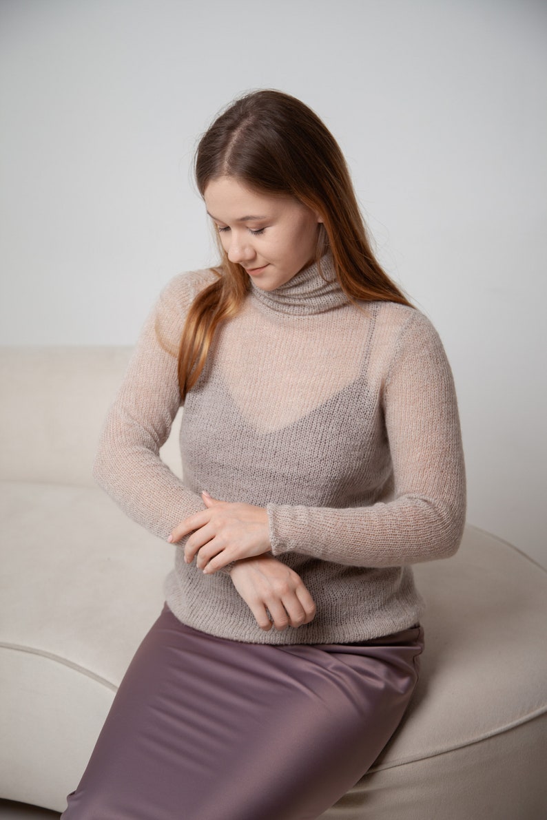 May include: A sheer, light brown turtleneck sweater with long sleeves. The sweater is paired with a dark purple satin skirt. The outfit is simple and elegant, suitable for layering or wearing on its own.