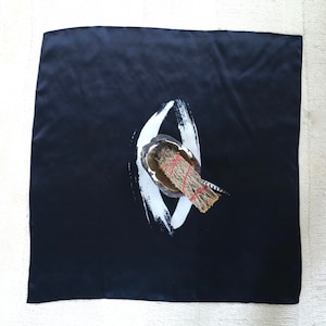 May include: A black square cloth with a white painted symbol in the center. A bundle of sage is placed on top of the symbol.