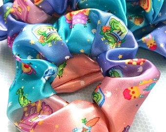 May include: A set of three colourful scrunchies featuring a whimsical pattern of houses, stars, and plants. The scrunchies are made from satin fabric and are ideal for adding a touch of personality to any hairstyle.