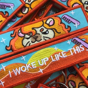May include: A set of colourful embroidered patches featuring a cartoon lion with a comb and the text "I woke up like this". The patches are orange, yellow, blue, and white.