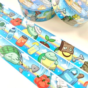 May include: Three rolls of washi tape with a blue background and a rainbow design. The tape features illustrations of turtles, a can of soda, a glass of lemonade, a plant, a bag of oranges, a fish bone, and a shovel. The text on the tape reads "Reduce Reuse Recycle" and "itsdilful washi tape".