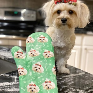 May include: A green oven mitt with a repeating pattern of a small white dog wearing a red bow. The dog's face is visible on the mitt.