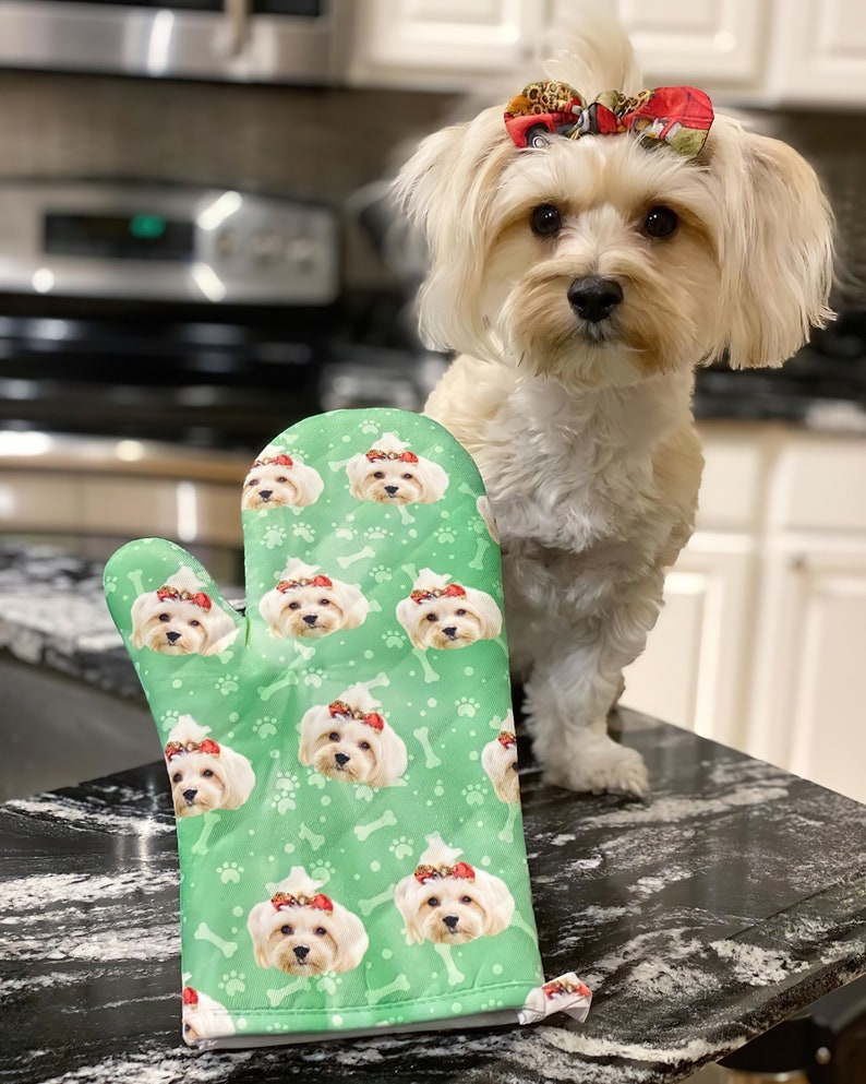 May include: A green oven mitt with a repeating pattern of a small white dog wearing a red bow. The dog's face is visible on the mitt.