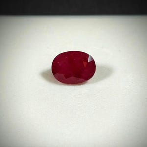Può includere: Una gemma di rubino sfaccettata, di forma ovale. La gemma è di un colore rosso intenso e ricco, con una visibile chiarezza interna. La pietra è posta su uno sfondo bianco, evidenziando la sua brillantezza. Adatta per gioielli.