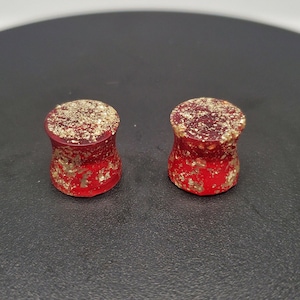 Puede incluir: Par de expansores de oreja rojos y dorados con un acabado moteado.