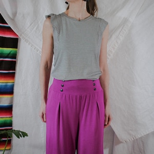 May include: A black and white striped sleeveless top and high-waisted magenta culottes. The culottes feature button detailing at the waist. The outfit is a contemporary take on a classic style.