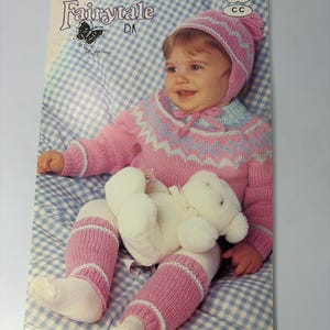 May include: A vintage knitting pattern booklet titled Patons Fairytale DK, number 488 CC, featuring a photograph of a child wearing a pink and blue patterned knit sweater, matching hat with a pom-pom, and leg warmers, holding a white plush toy.