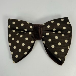 May include: A brown bow tie with a velvet center and white polka dots. This formal accessory is suitable for special occasions. The bow tie is approximately 5 inches wide.