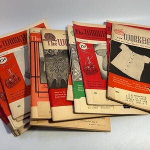 May include: A stack of vintage magazines titled "The Workbasket" with red and white covers. The magazines feature various craft projects, including knitting, crocheting, and sewing. The covers include illustrations of a crocheted butterfly, a knitted baby bonnet, and a crocheted bag.