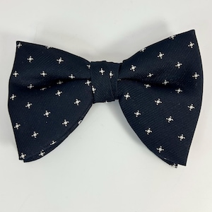 May include: A black bow tie with a repeating white floral pattern. The bow tie is made of a textured fabric and is tied in a classic bow shape. The bow tie is a formal accessory.