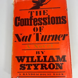 May include: A vintage book titled "The Confessions of Nat Turner" by William Styron. The cover is bright orange with black text and a graphic of a figure with a sword. A Random House Book is printed at the bottom.