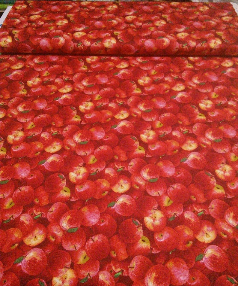 May include: Red fabric with a repeating pattern of red apples. The apples are arranged in a close-up, overlapping pattern.