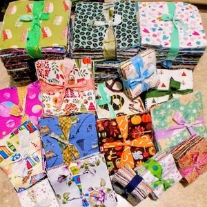 May include: A collection of multiple stacks of square fabric pieces, each bundle tied with a ribbon. The fabric squares feature various colourful patterns including coffee beans, hearts, autumn leaves, pumpkins, beach scenes, and floral designs.