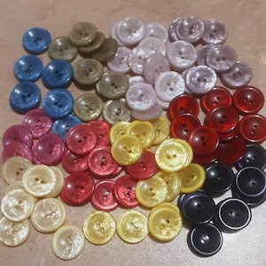 May include: Assortment of colourful buttons in various shades of blue, red, yellow, green, and white. The buttons are made of a shiny, iridescent material and have two holes.
