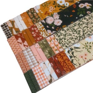 May include: A collection of fabric scraps in various patterns and colours, including floral, geometric, and plaid. The fabrics are arranged in a stack, with the top layer showing a floral pattern in shades of pink, orange, and green.
