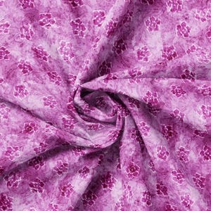 May include: A close-up of a pink fabric with a white floral pattern. The fabric is folded and twisted, creating a swirling effect.