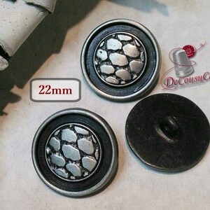 May include: Two silver-toned buttons with a black rim and a raised, textured design of gray stones. The buttons are 22mm in diameter. The back of one button is shown, revealing a black metal surface with a single hole.