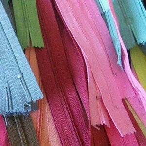 May include: Assortment of colorful zipper tapes in various shades of pink, blue, green, and brown. The zipper tapes are arranged in a layered pattern, showcasing the different colors and textures.