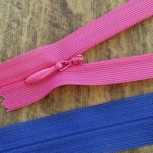 Pu&ograve; includere: Due nastri di cerniera, uno rosa e uno blu, sono mostrati su una superficie di legno. Il nastro di cerniera rosa ha un cursore rosa.