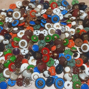 Peut inclure: Une grande collection de boutons de couture assortis de différentes couleurs, notamment rouge, bleu, vert, blanc, marron et noir. Les boutons présentent des designs variés, tels que des accents métalliques, des motifs en relief et des configurations de trous différentes.