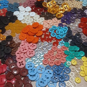 May include: A large collection of round plastic buttons in a variety of colors including red, orange, yellow, green, blue, pink, brown, black, white, and gold. Each button features four holes in the center for sewing attachment.