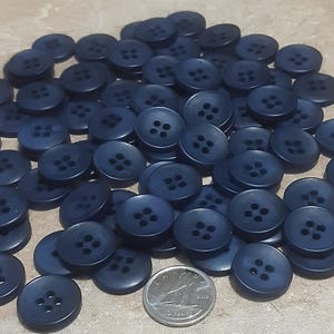 May include: A large pile of dark blue plastic buttons with four holes each. The buttons are arranged in a random pattern.