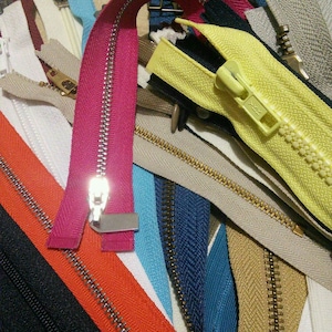 May include: A collection of colourful zipper tapes in various colours, including red, yellow, blue, black, and white. The zippers have metal teeth and are arranged in a random pattern.