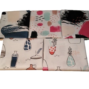 May include: Five folded fabric napkins with diverse patterns. Some have abstract brushstrokes in navy, black, pink, and teal on a white backdrop. Others show vase and plant illustrations in a minimalist style.