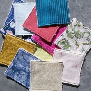 May include: A collection of 10 handmade fabric squares with various patterns and colors, including blue, green, yellow, pink, and white. The squares have a frayed edge and are likely intended for use as reusable makeup remover pads.