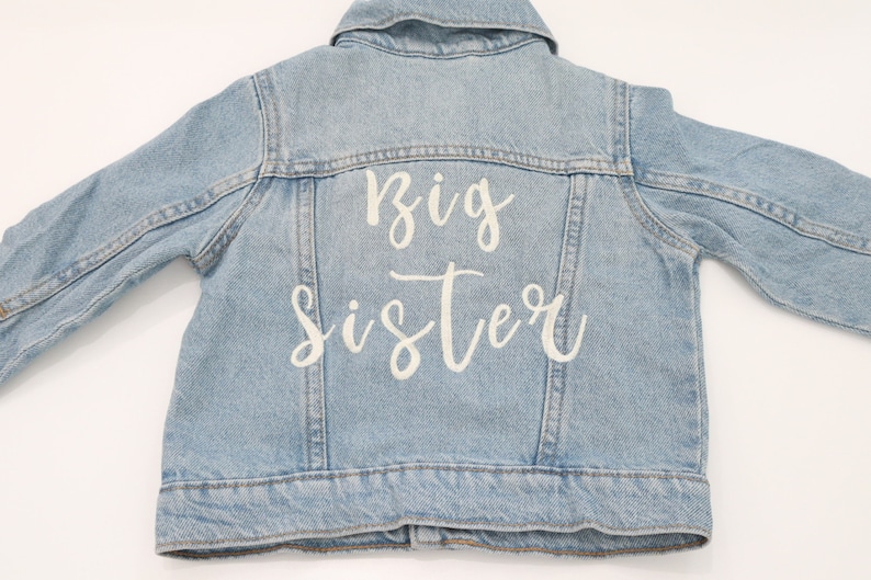 May include: A light blue denim jacket with the words "Big Sister" embroidered on the back in white.