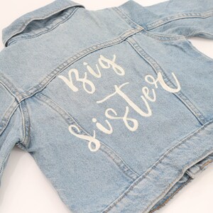 May include: A light blue denim jacket with white lettering on the back that says "Big Sister".