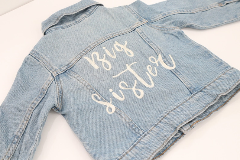 May include: A light blue denim jacket with white lettering on the back that says "Big Sister".