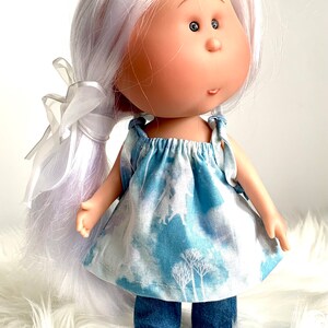 May include: A doll with long white hair, wearing a blue and white patterned dress and denim pants. The doll has large eyes and a sweet expression.