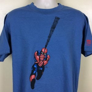 May include: A blue t-shirt with a graphic of Spider-Man swinging on a web. The graphic is in red, black, and white. The shirt has a Marvel Comics logo on the right sleeve.