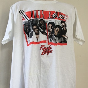May include: White t-shirt featuring a graphic of the group LeVert with the text "Jays LeVert" in red and the words "Rude Boys" in red. The shirt is displayed on a mannequin.