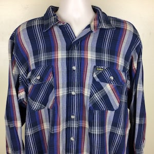 May include: A blue, red and white plaid long-sleeved button-down shirt with two chest pockets. The shirt has a label that reads "Gildan" in yellow letters.