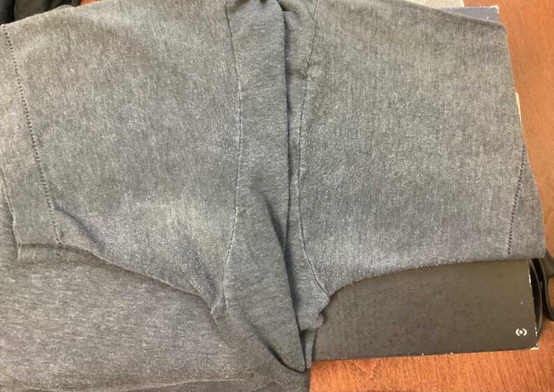 May include: A gray t-shirt with a faded look. The shirt is folded in half and the fabric is textured.