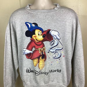May include: A light gray sweatshirt featuring a graphic of Mickey Mouse in a sorcerer's outfit, holding a wand and the number 25. The Walt Disney World logo is printed below the graphic.