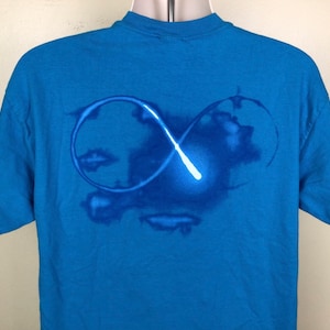 Könnte beinhalten: Ein blaues T-Shirt mit einem weißen Unendlichkeits-Symbol-Design. Das Symbol ist weiß umrandet und hat einen weißen Schein in der Mitte.