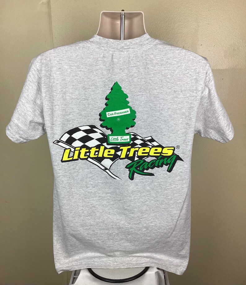 May include: A gray t-shirt with a green pine tree graphic and the text "Little Trees Racing" in yellow and black. The pine tree graphic has a white rectangle with the text "Car Freshener" on it.