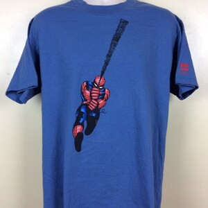 May include: A blue t-shirt with a graphic of Spider-Man swinging on a web. The shirt has a Marvel Comics logo on the right sleeve.
