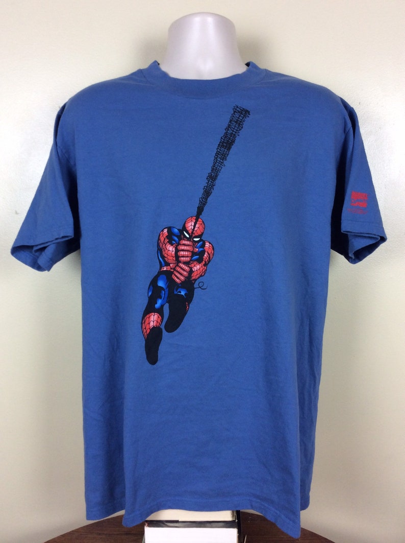 May include: A blue t-shirt with a graphic of Spider-Man swinging on a web. The shirt has a Marvel Comics logo on the right sleeve.