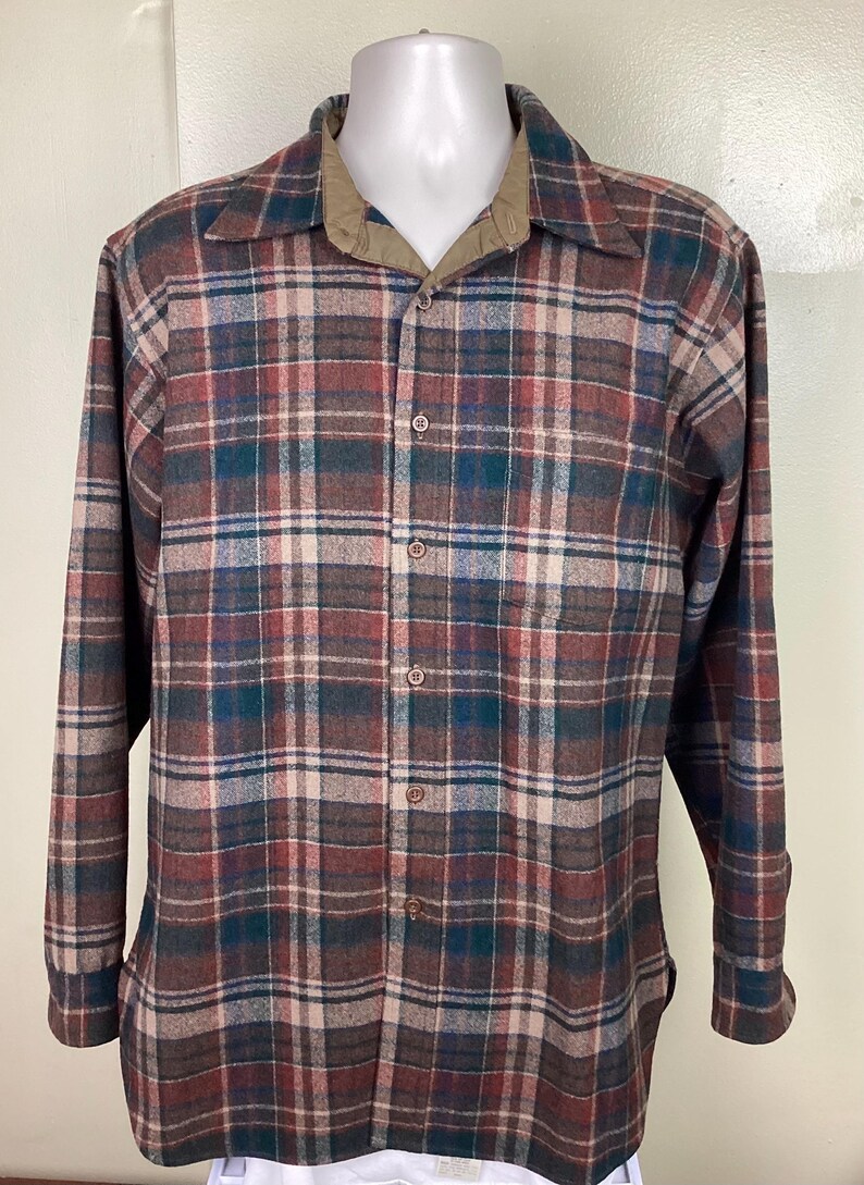 May include: A long-sleeved plaid shirt with a brown, red, green, and white plaid pattern. The shirt has a button-down collar and a button-up front.