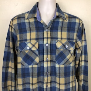 Op de afbeelding: Een langarm geblokt flanellen overhemd in blauw, geel en grijs. Het overhemd heeft een knoopsluiting en twee borstzakken.