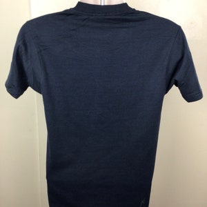 Pu&ograve; includere: Una maglietta nera a maniche corte con un piccolo logo bianco in basso a destra.