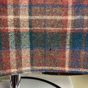 May include: Close-up of a brown, red, green, and blue plaid fabric. The fabric has a woven texture and is likely made of wool.