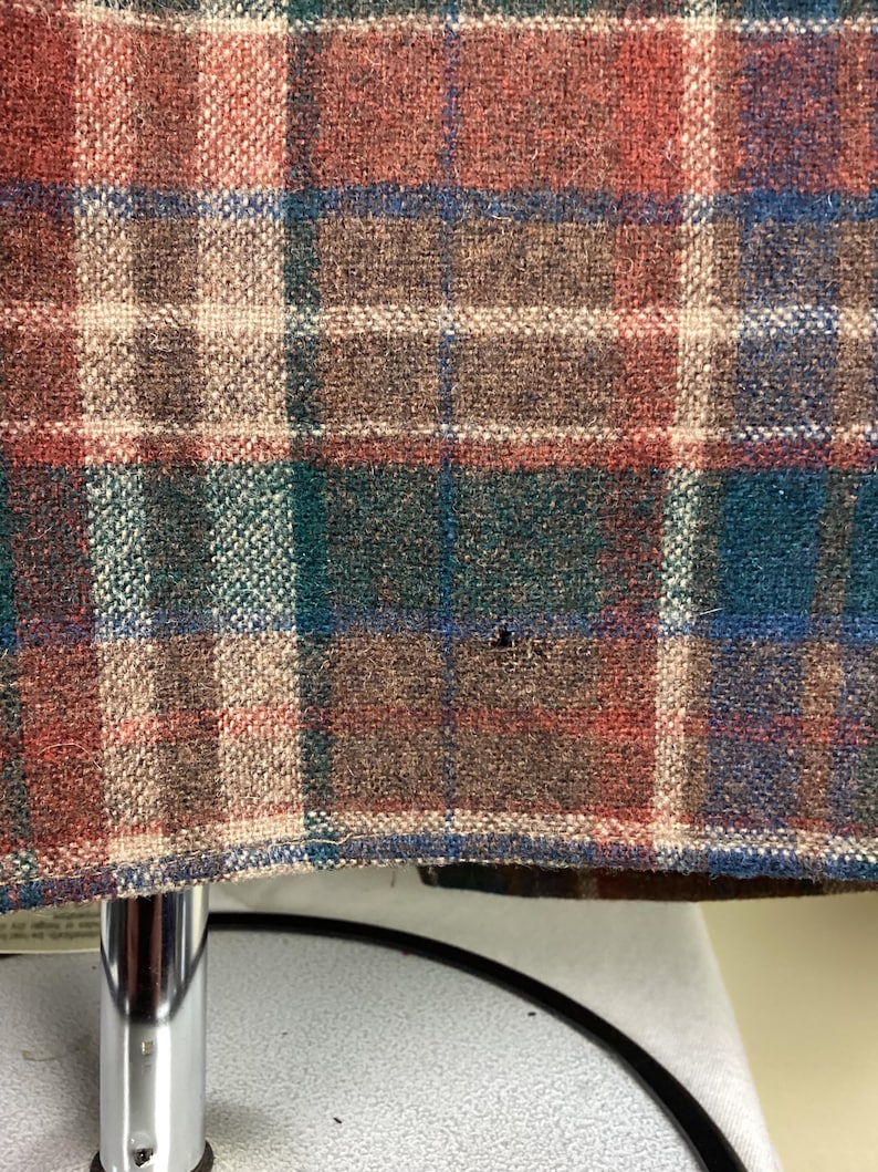 May include: Close-up of a brown, red, green, and blue plaid fabric. The fabric has a woven texture and is likely made of wool.