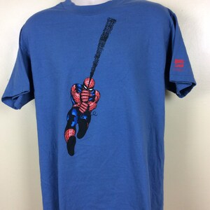 May include: A blue t-shirt with a graphic of Spiderman swinging on a web. The graphic is in red, black, and white. The t-shirt has a Marvel Comics logo on the bottom right corner.